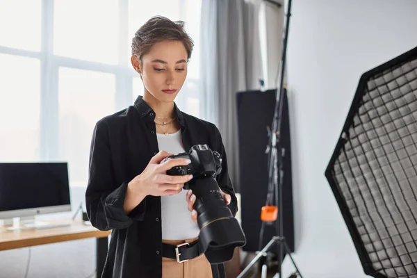 Молода приваблива жінка-фотограф в повсякденному вбранні дивиться на фотографії на її камеру в студії — стокове фото