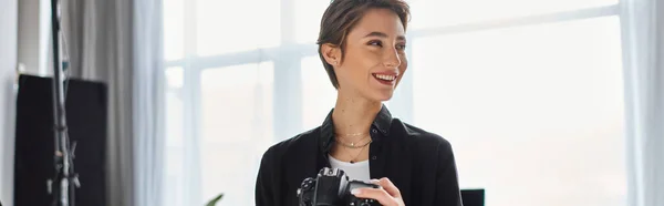 Fotógrafo feminino feliz em roupas casuais com câmera nas mãos sorrindo e olhando para longe, banner — Fotografia de Stock