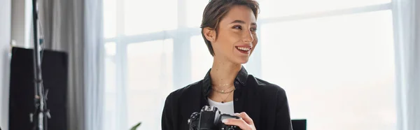 Glückliche Fotografin in lässiger Kleidung mit Kamera in den Händen, lächelnd und wegschauend, Banner — Stockfoto