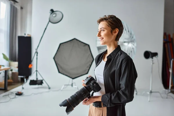 Jolly female photographer in casual outfit with camera in her hands smiling and looking away — Stock Photo