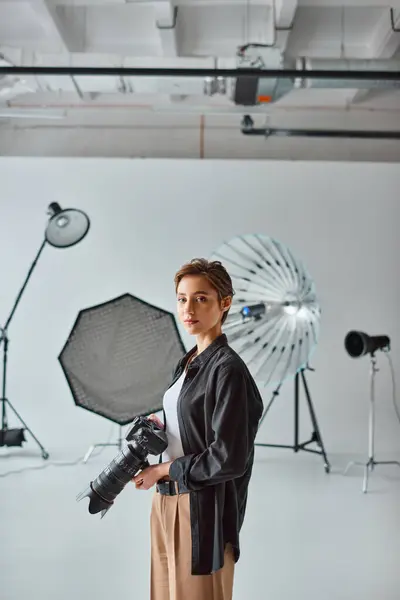 Attractive female photographer in casual attire looking at camera surrounded by her equipment — Stock Photo