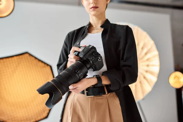 Visão recortada de jovem fotógrafa em traje casual trabalhando em estúdio com vários equipamentos — Fotografia de Stock