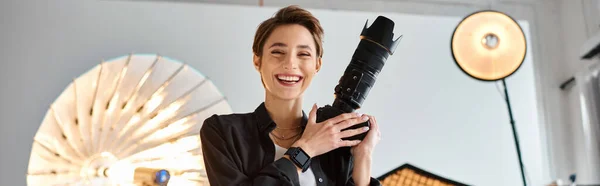 Belle femme joyeuse dans les vêtements de tous les jours posant dans son studio avec caméra dans les mains, bannière — Photo de stock