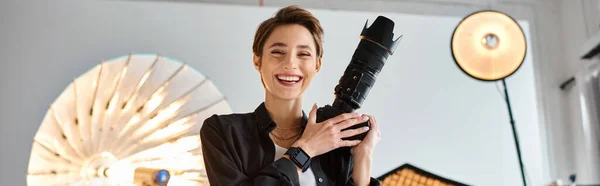 Beautiful jolly woman in everyday clothing posing in her studio with camera in hands, banner — Stock Photo