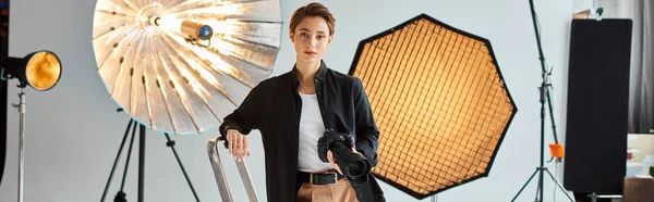 Jovem fotógrafa atraente em traje casual olhando para a câmera enquanto em seu estúdio, banner — Fotografia de Stock