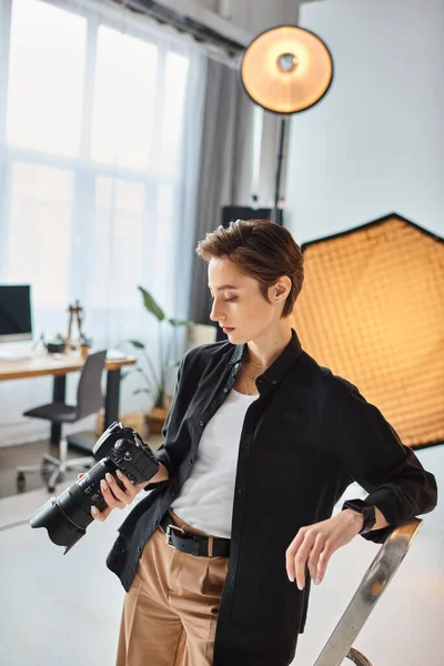 Young attractive woman with short hair in casual attire looking at photos on her camera in studio — Stock Photo