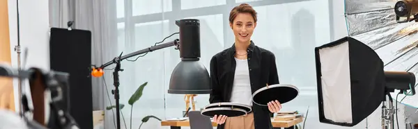Jolly beautiful woman with short hair posing with her photography equipment in her studio, banner — Stock Photo