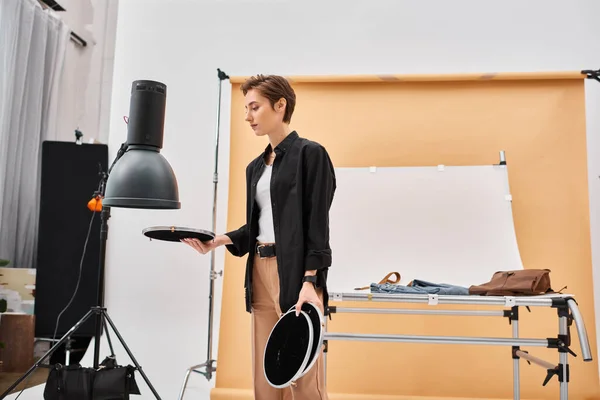 Good looking short haired female photographer in casual attire working with her equipment at studio — Stock Photo