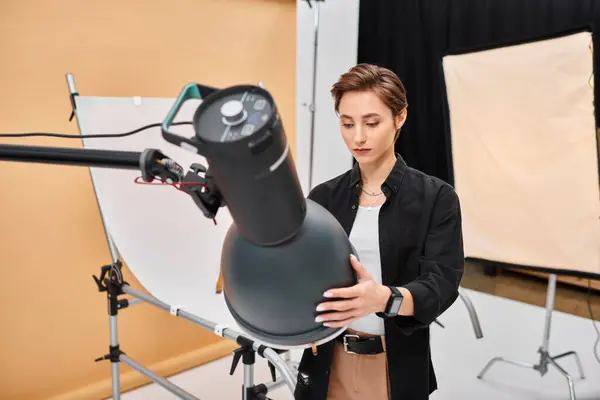 Superbe photographe aux cheveux courts en tenue décontractée travaillant avec son équipement en studio — Photo de stock