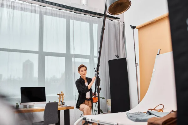 Bela fotógrafa de cabelos curtos em traje casual trabalhando com seu equipamento no estúdio — Fotografia de Stock