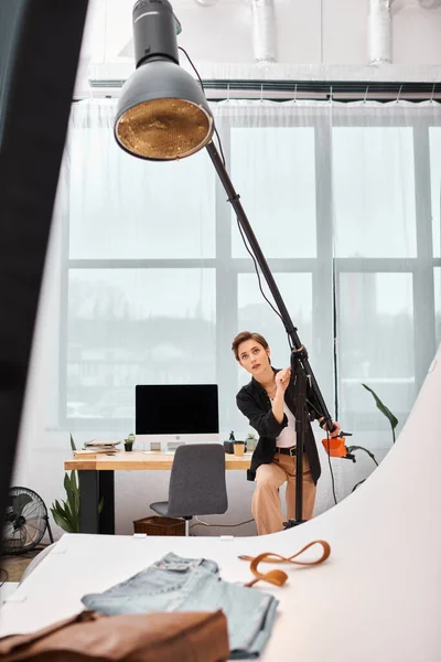 Charmante photographe aux cheveux courts en tenue décontractée travaillant avec son équipement en studio — Photo de stock