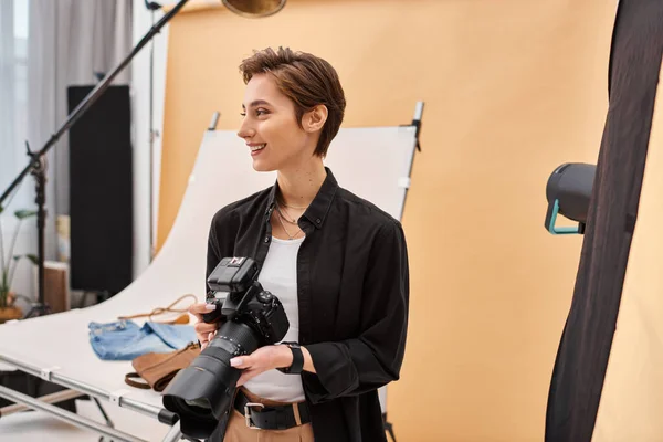 Alegre bela fotógrafa feminina em roupas cotidianas trabalhando com seu equipamento no estúdio — Fotografia de Stock