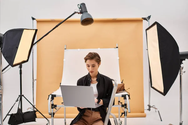 Atraente fotógrafo de cabelos curtos sentado e retocando fotos em seu estúdio usando seu laptop — Fotografia de Stock