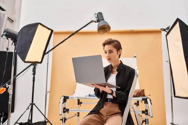 Belle photographe aux cheveux courts assis et retoucher des photos dans son studio en utilisant son ordinateur portable — Photo de stock