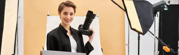 Allegra bella donna sorridente felicemente mentre ritocca le foto e tiene la sua macchina fotografica in studio, banner — Foto stock
