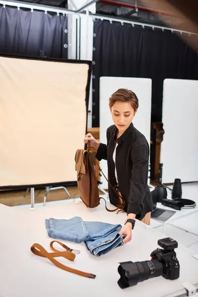 Чарівна короткошерста жінка-фотограф готується робити фотографії джинсів і коричневого рюкзака — стокове фото