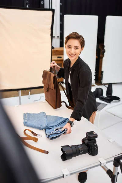 Allegro fotografo femminile che si prepara a fare foto di jeans e zaino e sorridente alla fotocamera — Foto stock