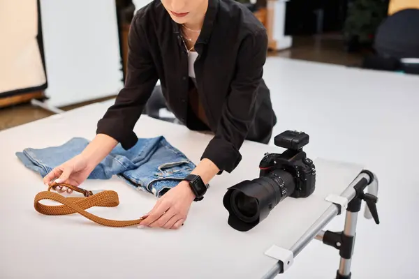 Cropped view of young female photographer preparing to make object photos of jeans and belt — Stock Photo