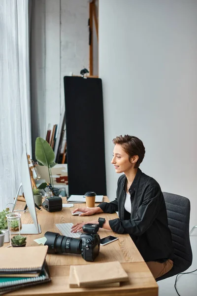 Cheerful professional female photographer in casual wear retouching photos on computer at her studio — Stock Photo