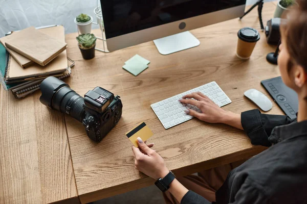 Cropped view of young female photographer sitting at table using credit card to pay online — Stock Photo