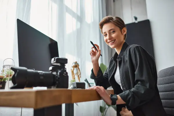 Femme gaie travaillant avec tablette de dessin et son appareil photo devant l'ordinateur et souriant joyeusement — Photo de stock