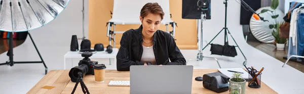 Attractive female photographer in casual attire working at laptop with coffee cup on table, banner — Stock Photo