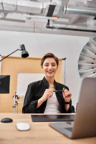 Attractive cheerful short haired woman in casual attire working in studio and having much fun — Stock Photo