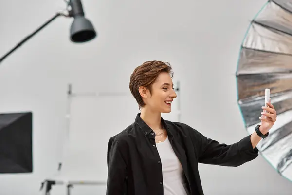 Jolly charming woman with in casual attire with short hair making stories for social media in studio — Stock Photo