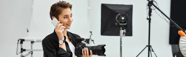 Jolly attractive female photographer with camera in her hands talking by her mobile phone, banner — Stock Photo