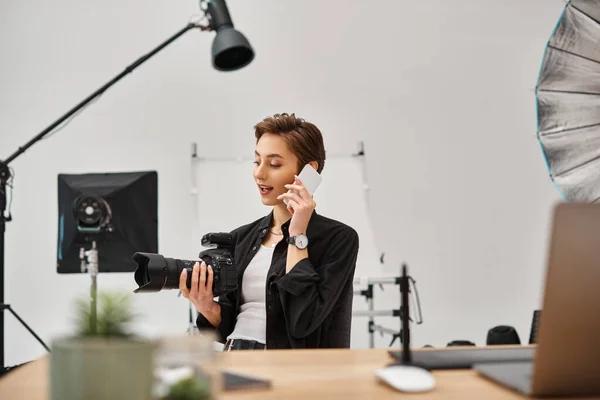 Cheerful attractive female photographer with camera in her hands talking by her mobile phone — Stock Photo