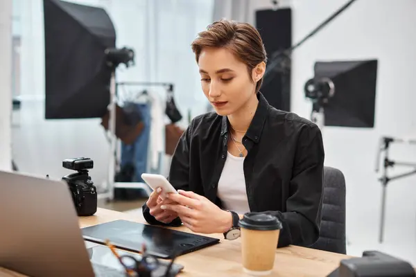 Atractiva joven mujer de pelo corto con teléfono inteligente en sus manos mientras trabaja en un estudio de fotografía - foto de stock