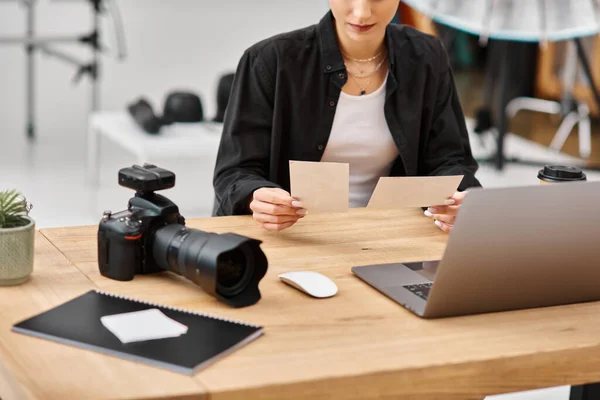 Vista recortada de la joven fotógrafa sentada en la mesa y mirando fotos en sus manos - foto de stock