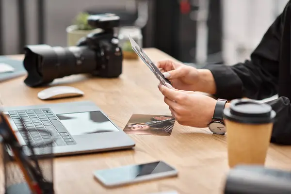 Cropped view of camera and coffee on table next to young female photographer with photos in hands — Stock Photo