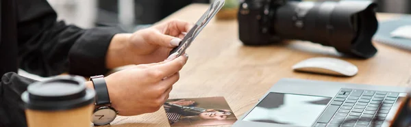 Vista recortada de la joven fotógrafa sosteniendo fotos en las manos mientras está sentada en la mesa, pancarta - foto de stock