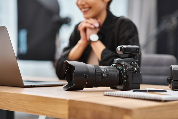 Cropped focused view on camera on table next to cheerful blurred female photographer with wristwatch — Stock Photo