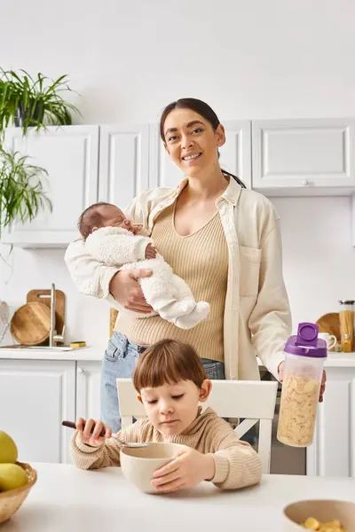Jolly beautiful mother enjoying breakfast with her toddler and newborn sons, modern parenting — Stock Photo