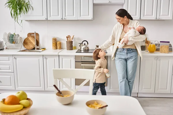 Caring jolly mother in housewear spending time with her toddler and newborn sons during breakfast — Stock Photo