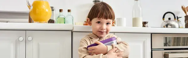 Cute toddler boy in homewear holding pack of corn flakes during breakfast on kitchen, banner — Stock Photo