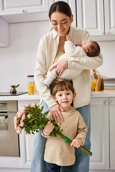 Famille gaie attentionnée en tenue de maison posant avec bouquet de fleurs tout en cuisine, parentalité moderne — Photo de stock