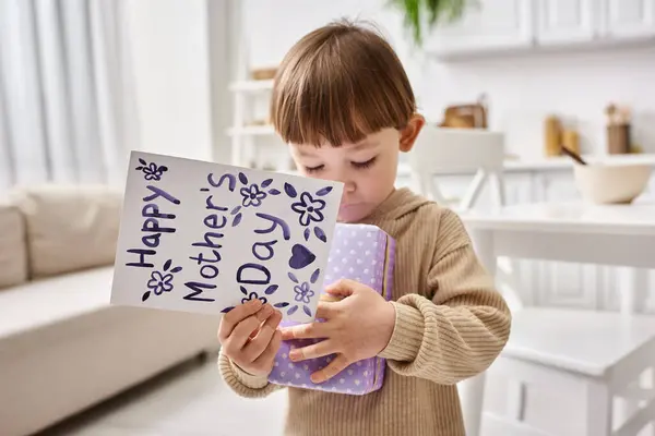 Adorable cute little boy in comfy homewear posing with present and greeting card on Mothers day — Stock Photo
