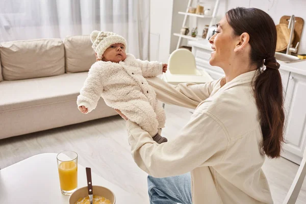 Feliz hermosa mujer en ropa de casa sosteniendo su lindo bebé niño durante el desayuno, crianza moderna - foto de stock