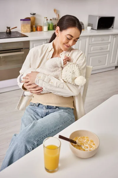 Joyeux belle femme en tenue de maison tenant son mignon bébé garçon pendant le petit déjeuner, parentalité moderne — Photo de stock