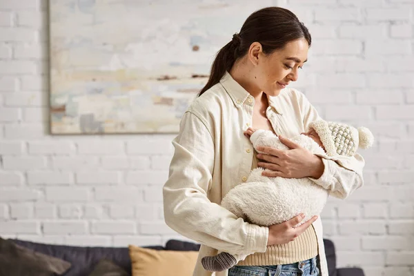Atractiva madre feliz en ropa de casa casual posando con su bebé en las manos, crianza moderna - foto de stock