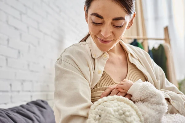 Schöne fürsorgliche fröhliche Mutter in gemütlicher Hauskleidung, die ihr neugeborenes Kind stillt, moderne Elternschaft — Stockfoto