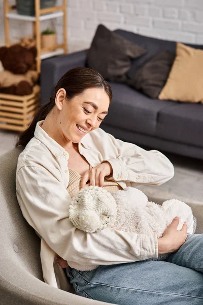 Красивая веселая женщина в пастельном домашнем платье с джинсами сидя и кормя грудью своего малыша — стоковое фото