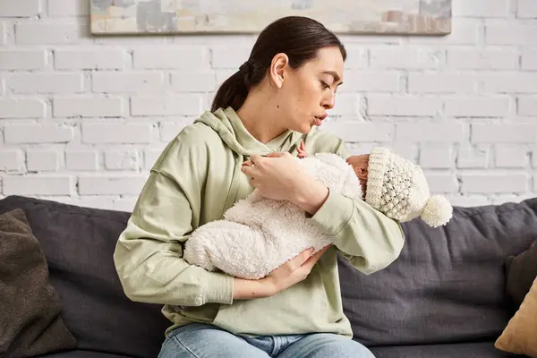 Good looking loving mother in homewear comforting her cute newborn baby on sofa, modern parenting — Stock Photo