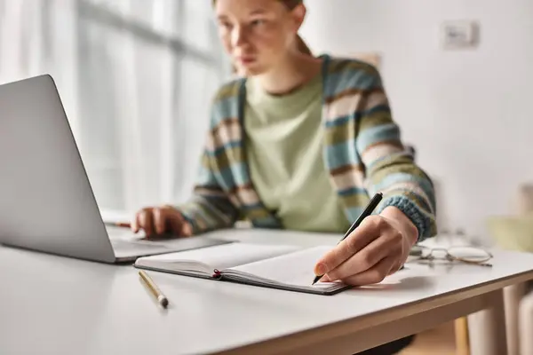 Focused teenager doing homework on laptop in a home environment, focus on gen z girl taking notes — Stock Photo