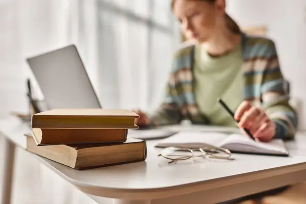 Se concentrer sur les livres sur le bureau, adolescente tenant stylo et regardant ordinateur portable tout en étudiant de la maison — Photo de stock