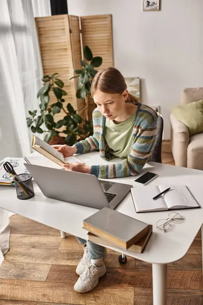 Gen z menina segurando livro ao usar um laptop para e-learning em casa, conceito de estilo de vida adolescente — Fotografia de Stock