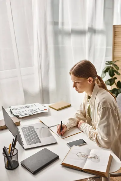 Teenage girl writing in notebook and looking at laptop while doing her homework, online learning — Stock Photo